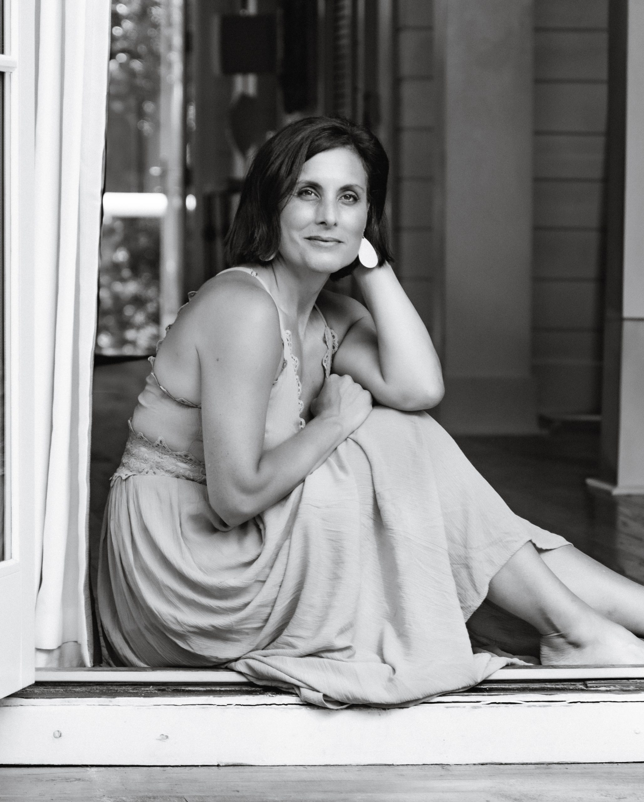Black and white portrait of woman seated in doorway wearing flowing dress, natural light photography by Tammy Jaquith in Oregon