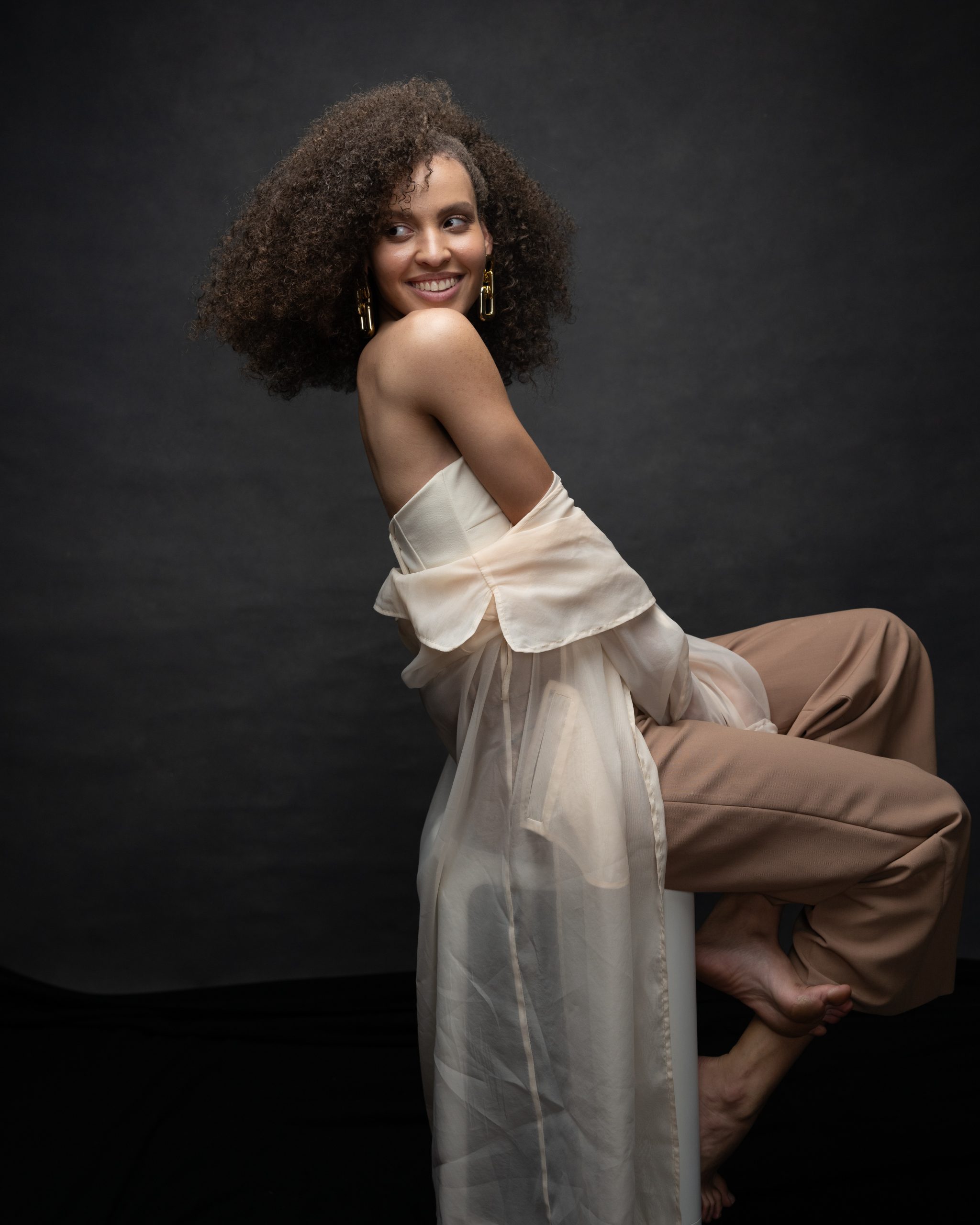 Joyful portrait of woman with natural curls in sheer cream top, laughing and looking over shoulder, studio photography by Tammy Jaquith in Oregon