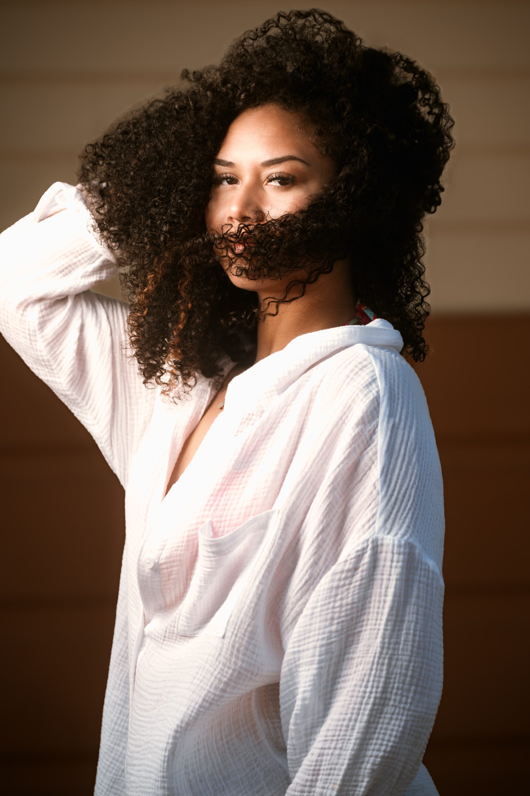 Woman with natural curls in white muslin top, warm golden light catching her hair, relaxed studio portrait by Tammy Jaquith Photography in Oregon