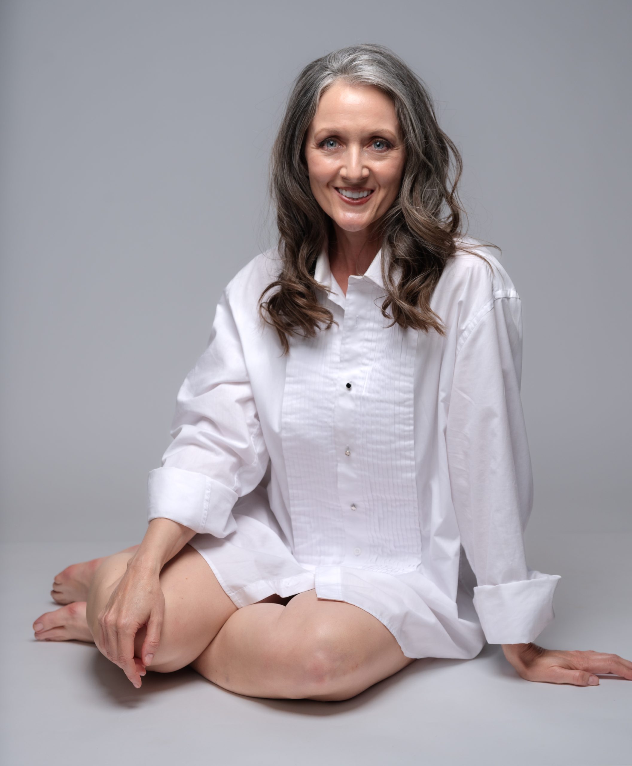 Woman with natural silver hair in classic white shirt, seated and smiling, studio portrait by Tammy Jaquith Photography in Oregon's Willamette Valley